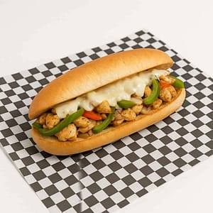 Hyper-realistic Chicken Philly Hero on check deli paper with tender seasoned chicken, grilled peppers, onions, and melted mozzarella cheese on a toasted hero roll. Perfect chicken cheesesteak or lunch near me in Newport News.